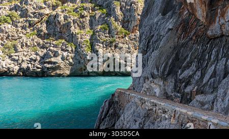 Un sentier de pierre pittoresque courbe le long de falaises rocheuses abruptes au-dessus des eaux bleues vives de sa Calobra sur la côte nord-ouest de Majorque, en Espagne. Banque D'Images