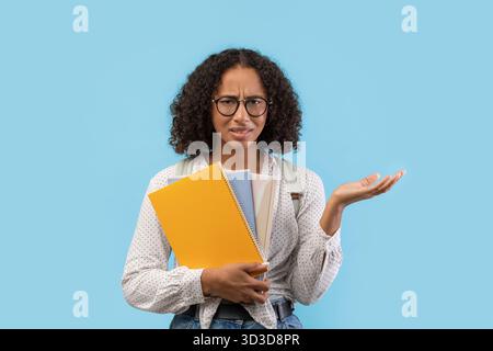 Étudiante noire frustrée luttant avec les devoirs sur fond bleu Banque D'Images