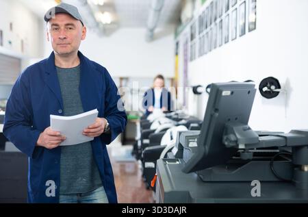 Portrait d'un employé de la maison d'impression avec pile de papier dans ses mains Banque D'Images