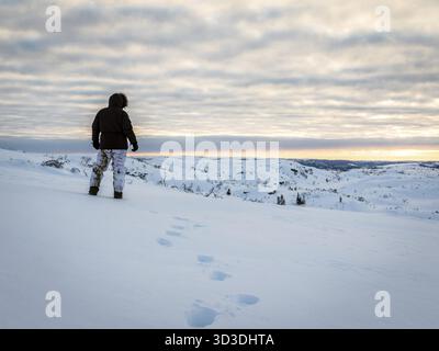 Homme seul marchant dans la neige dans la nature sauvage au lever du soleil. Vêtements d'hiver chauds et pantalons camouflage d'hiver. Beau ciel avec des nuages tôt le matin Banque D'Images