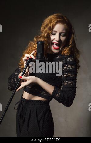 Close-up of red-haired woman signature chanson dans mic.Studio shot Banque D'Images