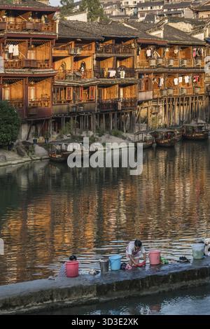 Feng Huang, Chine - août 2019 : femmes faisant la lessive sur le rivage devant les vieilles maisons historiques sur pilotis en bois sur les rives de la rivière Tuo, fl Banque D'Images