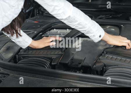 Jeune femme debout devant la voiture avec le capot ouvert regardant sous un capot de voiture Banque D'Images