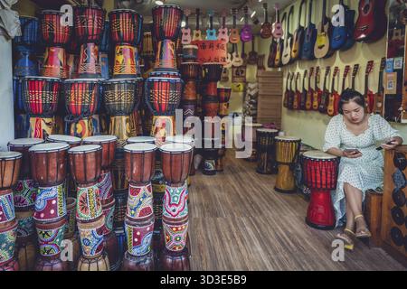 Feng Huang, Chine - août 2019 : vendeuse ennuyée attendant des clients à l'intérieur de son instrument traditionnel et magasin de musique dans la rue dans l'ol Banque D'Images