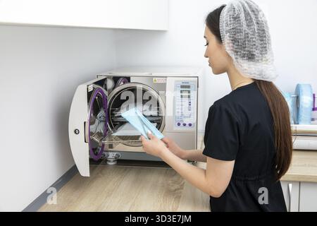 Stérilisation d'instruments médicaux en autoclave. Cabinet dentaire. Les mains de l'assistant dentiste sortent stérilisant les instruments médicaux de l'autoclave Banque D'Images