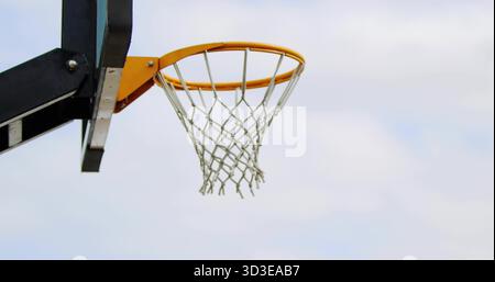 Montrant un panier de basket-ball avec un rebord orange et un filet blanc sur la cour extérieure gauche, espace copie Banque D'Images
