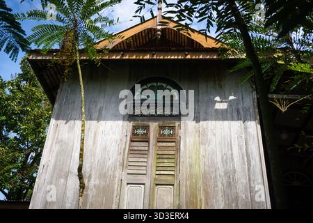 Une maison malaise en bois se dresse tranquillement sous la lumière tropicale, ses panneaux sculptés et ses bois altérés abritant des histoires de foi, de famille et de temps Banque D'Images