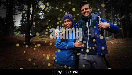 Couple souriant se promenant sous les feuilles persistantes avec sac à dos, bonnet en tricot, foulards et partic clair doré Banque D'Images