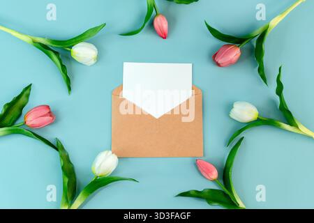 Une enveloppe avec une feuille blanche blanche pour écrire sur un fond bleu entouré de tulipes printanières, un endroit pour le texte Banque D'Images
