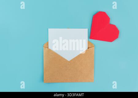 Une enveloppe avec une feuille blanche pour l'écriture et un coeur origami sur fond bleu, un endroit pour le texte Banque D'Images