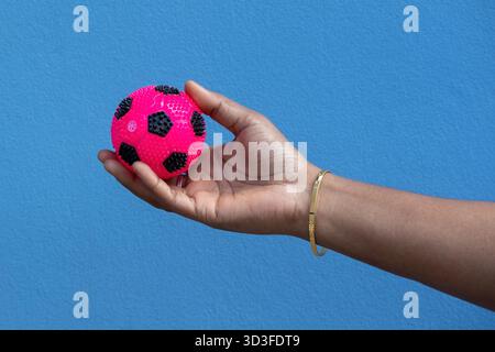 Gros plan, photo focalisée d'une main féminine tenant doucement une balle souple, ronde et colorée rebondissante, un jouet grinçant populaire pour les enfants ou les animaux de compagnie, ag Banque D'Images