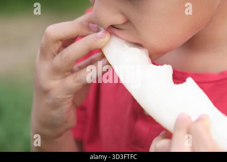 Plan détaillé capturant le plaisir d'un enfant à mordre dans un melon juteux, mettant en valeur les textures et les couleurs vives. Favorise le plaisir de manger Banque D'Images