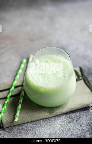 Un latte matcha rafraîchissant dans un verre, garni de mousse de lait. La boisson verte vibrante est complétée par deux pailles de papier vert, photographiées sur un Banque D'Images