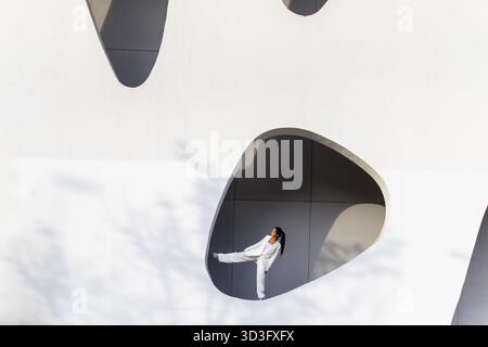 Femme d'affaires dans un cadre urbain blanc moderne, debout avec confiance dans un espace architectural artistique, symbolisant l'innovation et les profes contemporains Banque D'Images