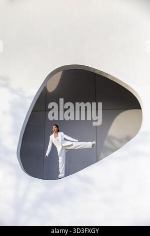 Une femme d'affaires en costume blanc se tient confiante dans un cadre urbain moderne, alliant élégance et professionnalisme. L'architecture blanche améliore Banque D'Images