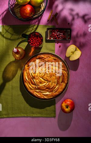 Vue de dessus d'une tarte aux pommes maison magnifiquement arrangée sur une table vibrante. La tarte présente une croûte dorée avec des tranches de pomme soigneusement superposées, surroun Banque D'Images