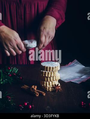 Les mains recadrées d'une femme méconnaissable enveloppent des polvorones d'amande de Noël sur une table en bois sombre avec de l'anis étoilé, de la cannelle et de la verdure festive pour les vacances Banque D'Images