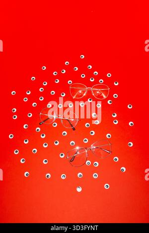 Une image conceptuelle vibrante avec trois lunettes entourées de nombreux petits yeux sur un fond rouge frappant, symbolisant la vision et la perceptio Banque D'Images