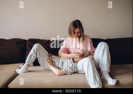 Une mère aimante partage un moment tendre avec sa fille atteinte du syndrome de Down. Ils sont assis confortablement sur le canapé, appréciant la compagnie de l'autre Banque D'Images