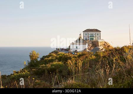 Vue panoramique d'un phare historique perché sur la côte accidentée de Galice, Espagne, surplombant le vaste océan Atlantique. Les touristes se rassemblent pour profiter du Banque D'Images