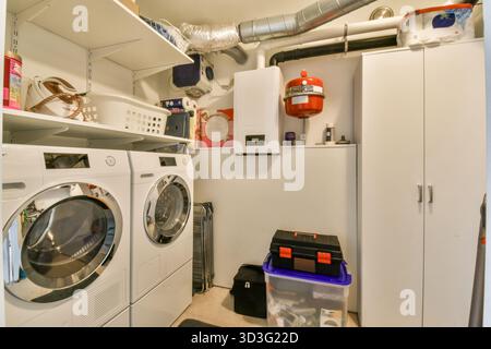 Une buanderie bien organisée avec des appareils blancs, des solutions de rangement et des éléments de décoration modernes. L'espace est fonctionnel avec équipement supplémentaire Banque D'Images