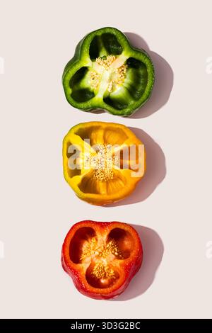 Une image frappante mettant en vedette trois poivrons tranchés dans des tons verts, jaunes et rouges vifs, soigneusement disposés sur un fond lisse et neutre. Parfait f Banque D'Images