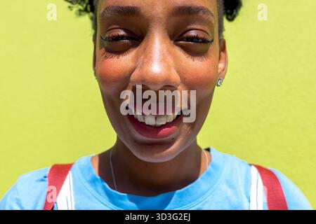 Gros plan d'une femme souriante sur un fond vert citron vibrant. Elle porte une chemise bleue, profitant de la journée ensoleillée avec une expression joyeuse Banque D'Images