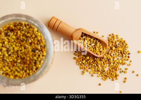 Vue de dessus de granules de pollen d'abeille naturel dans un bocal en verre avec une pelle en bois sur un fond beige. Idéal pour promouvoir le bien-être, la nutrition et une guérison Banque D'Images