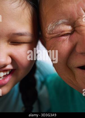 Un gros plan chaleureux d'un homme âgé et de sa petite-fille riant ensemble, mettant en valeur leurs expressions joyeuses et leur lien profond dans un setti familial Banque D'Images