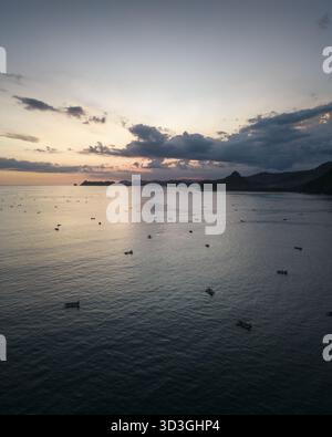 Vue aérienne de l'océan tranquille parsemé de petits bateaux sous un ciel doux aux couleurs pastel, Lombok, West Nusa Tenggara, Indonésie. Banque D'Images