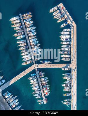 Vue aérienne de nombreux bateaux amarrés côte à côte dans un port structuré, leurs coques blanches contrastant avec la mer bleu profond, Croatie. Banque D'Images