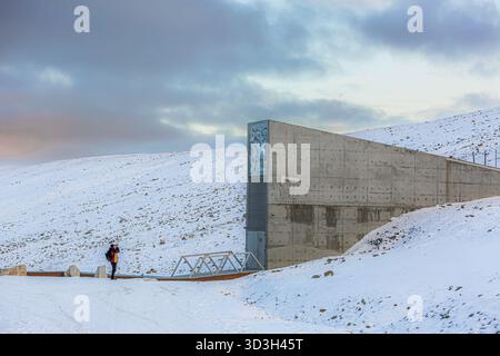 Longyerbeyen, Svalbard, l'homme est debout dans la neige à côté d'une grande structure en béton. Le ciel est nuageux et la neige s'accumule sur le sol. Le Banque D'Images