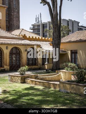 Vue sur l'architecture jaune complexe et les vieux murs de pierre juxtaposés avec des bâtiments modernes et un grand arbre jetant des ombres sur la pelouse, Cascais, L. Banque D'Images