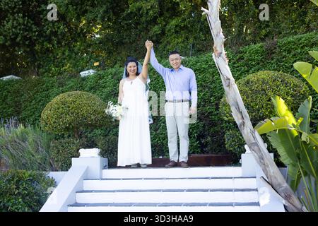 Couple senior célébrant à l'extérieur, se tenant la main et souriant sur les marches du jardin. Personnes âgées, bonheur, style de vie, relation, ensemble, amour || autorisation du modèle Banque D'Images