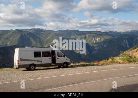 Camping-car garé sur une route de montagne avec vue panoramique sur les vallées verdoyantes et le paysage de montagne accidenté sous un ciel partiellement nuageux. Banque D'Images