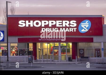 Calgary, Alberta, Canada. 23 mars 2025. Un magasin Shoppers Drug Mart au crépuscule, avec une vitrine illuminée en rouge et blanc avec le lo de la société Banque D'Images