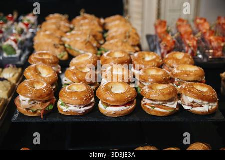 Nourriture, gros plan de mini sandwichs bagels au sésame remplis de dinde, fromage à la crème et légumes, disposés sur un plateau de restauration noir Banque D'Images