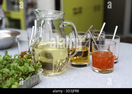 Nourriture, Une sélection de sauces dans des tasses en verre, y compris des liquides jaunes, oranges et clairs, avec des herbes fraîches au premier plan sur un comptoir de cuisine Banque D'Images