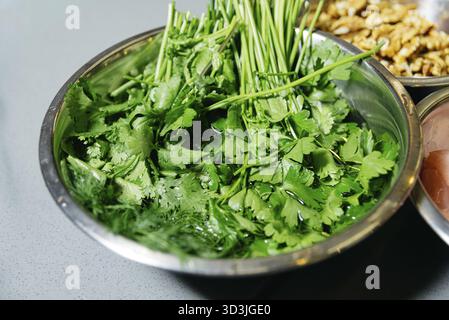 Nourriture, herbes vertes comme le persil et la coriandre lavées dans un bol en métal, préparées pour être utilisées dans la cuisson ou la préparation de salades Banque D'Images