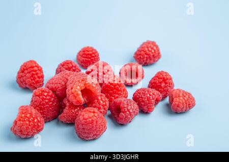 Framboises rouges éclatantes dispersées sur un fond bleu minimaliste, gros plan Banque D'Images