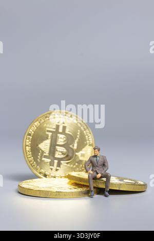 Homme d'affaires de personnes miniatures assis sur Bitcoin coins, concept d'investissement futur Banque D'Images