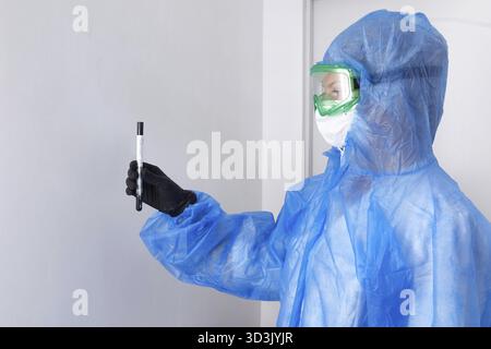 Technologue en soins médicaux tenant un écouvillon COVID-19, portant un vêtement de protection EPI, un masque, des gants. Tube à essai pour prélever un échantillon patient OP NP. Banque D'Images