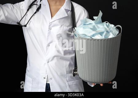 Docteur tenant seau plein de masques faciaux usagés, concept de lutte contre les virus avec poubelle Banque D'Images