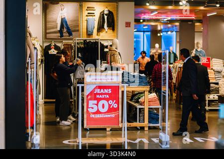 Les clients qui achètent des jeans et des vêtements décontractés dans un magasin de détail avec un panneau de réduction visible de 50 % dans le centre commercial. Banque D'Images