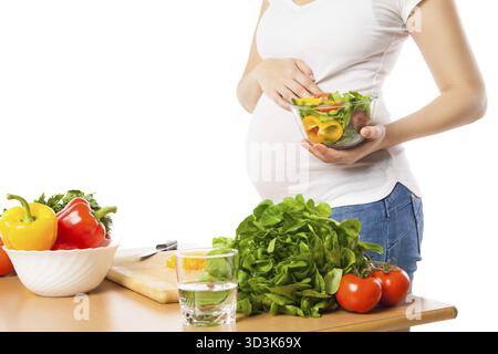 Femme enceinte méconnaissable avec bol de légumes frais à la table de la cuisine Banque D'Images