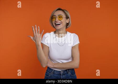Femme riante en t-shirt blanc et jeans montrant cinq doigts nombre isolé sur fond orange Banque D'Images