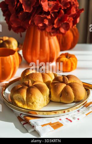 Table d'automne avec petits pains en forme de citrouille, cannelle, tasse, fleurs et décoration saisonnière. Banque D'Images