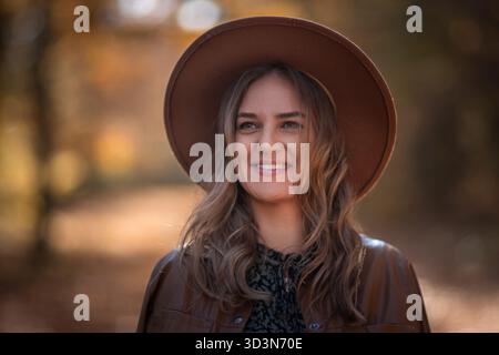 Femme chapeau Portrait d'automne : femme souriante chapeau brun à l'extérieur fond de feuillage d'automne. Banque D'Images