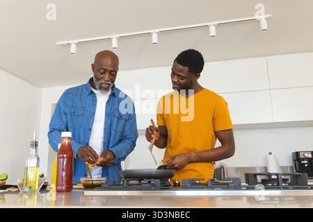Cuisine afro-américaine père et fils préparant le dîner dans la cuisine maison, avec poêle à frire Banque D'Images