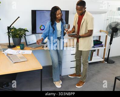 Examen des données collègues afro-américains dans un bureau moderne, avec smartphone et ordinateurs portables Banque D'Images